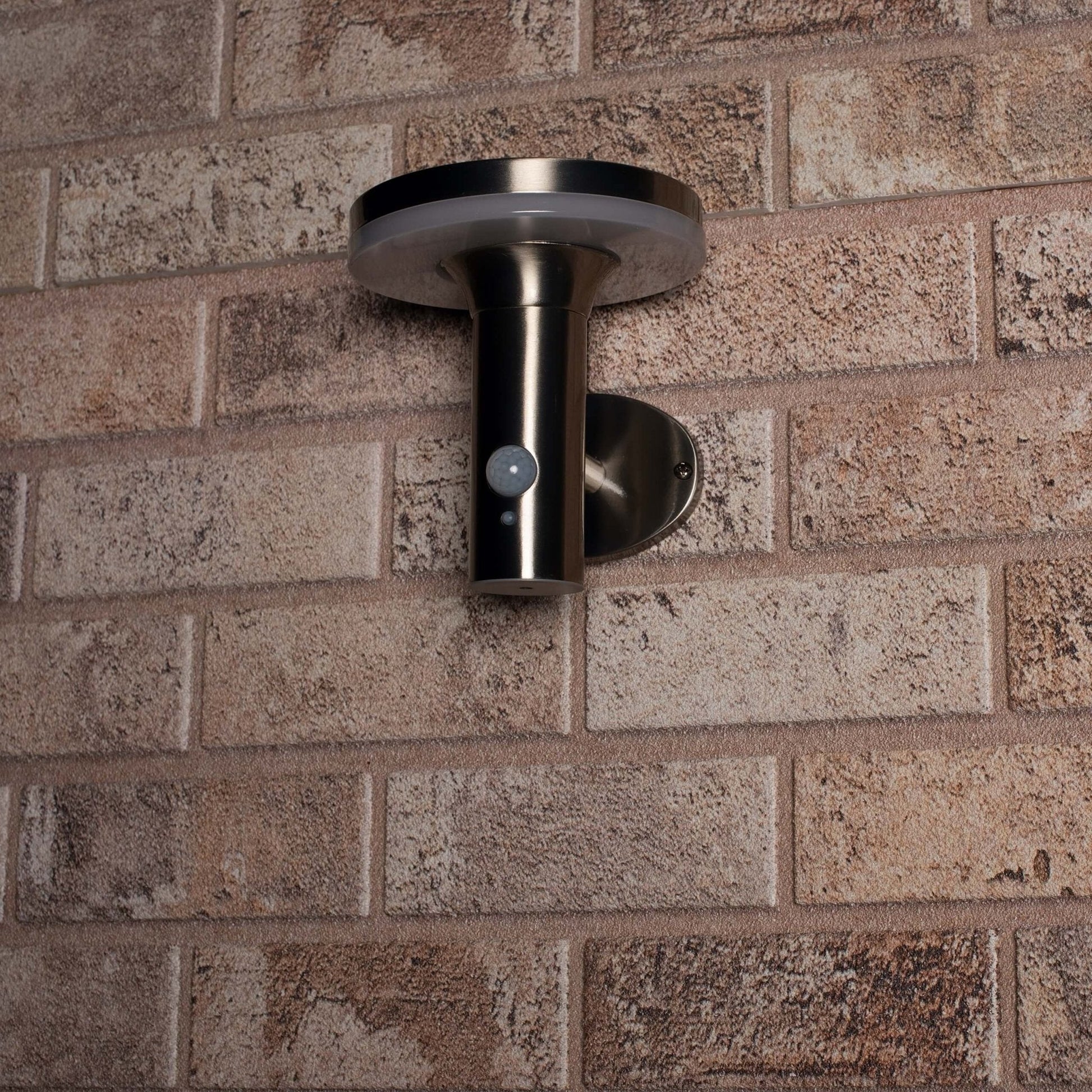Zachte, warme LED-verlichting met bewegingssensor, geïnstalleerd op een textuurrijke bakstenen muur. Modern, zilverkleurig ontwerp voor veilige buitenverlichting en nachtverlichting.