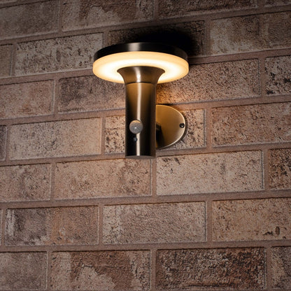 Zachte, warme LED-verlichting met bewegingssensor, geïnstalleerd op een textuurrijke bakstenen muur. Modern ontwerp in mat zwart, perfect voor buitenverlichting en veiligheid.
