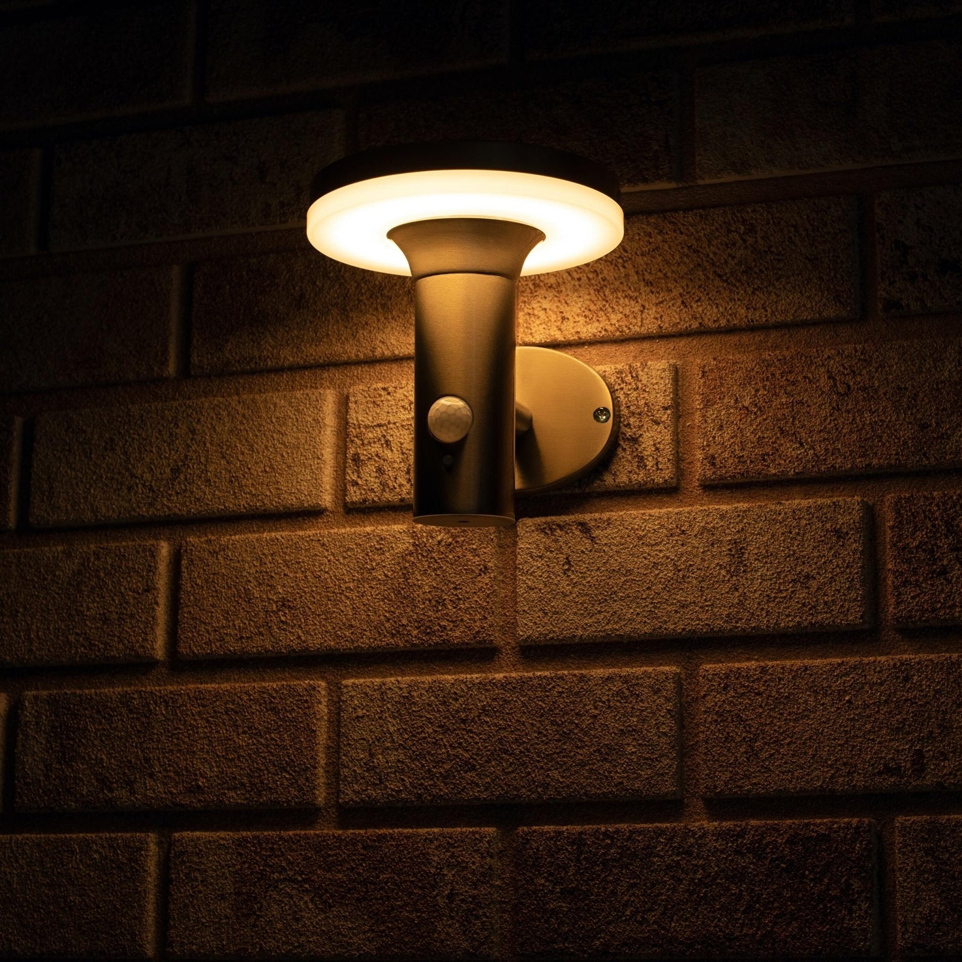 Zachte, warme LED-verlichting met bewegingssensor, geïnstalleerd op een textuurrijke bakstenen muur. Modern, zilverkleurig ontwerp voor veilige buitenverlichting en nachtverlichting.