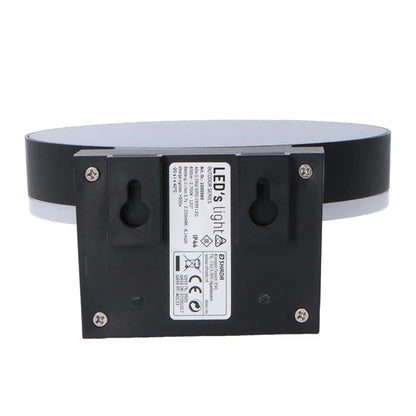 Een moderne, zwarte ringvormige wandlamp met warm wit licht, gemonteerd op een textuurrijke bakstenen muur. Uitgerust met bewegingssensor en aan/uit knop voor automatische verlichting in de entree of gang.