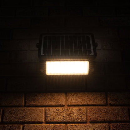 Zwarte zonnepanelenverlichting met warm wit licht, gemonteerd op een bakstenen muur. Ideaal voor buitenverlichting en tuinverlichting, met zichtbare LED’s en zonnecel.