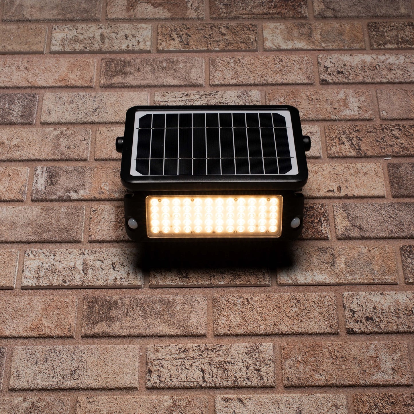 Zwarte zonnepanelenverlichting met warm wit licht, gemonteerd op een bakstenen muur. Ideaal voor buitenverlichting en tuinverlichting, met zichtbare LED’s en zonnecellen.
