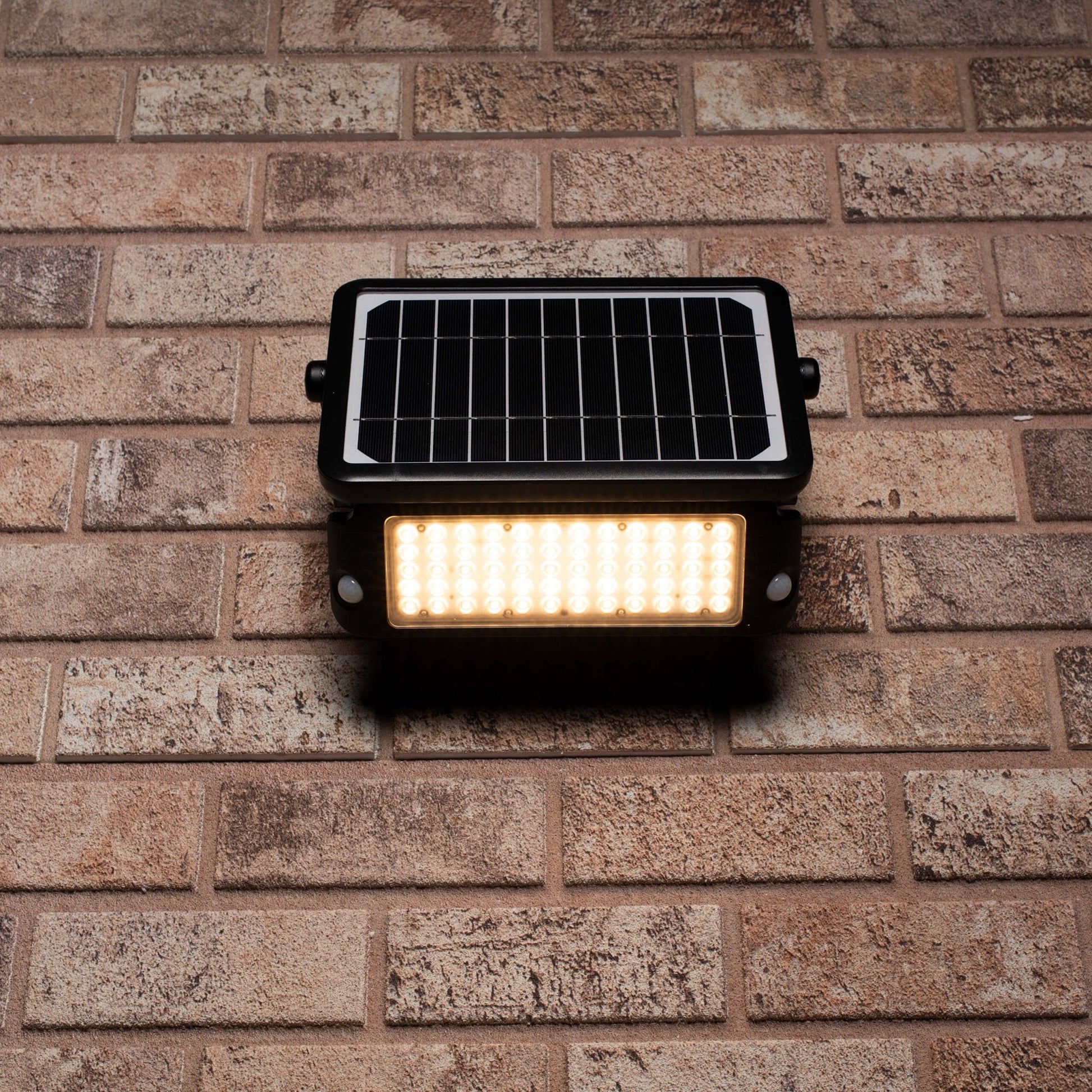 Zwarte zonnepanelenverlichting met warm wit licht, gemonteerd op een bakstenen muur. Ideaal voor buitenverlichting en tuinverlichting, met zichtbare LED’s en zonnecellen.