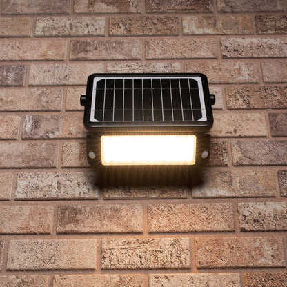 Zwarte zonnepanelenverlichting met warm wit licht, gemonteerd op een bakstenen muur. Ideaal voor buitenverlichting en tuinverlichting, met zichtbare LED’s en zonnecellen.