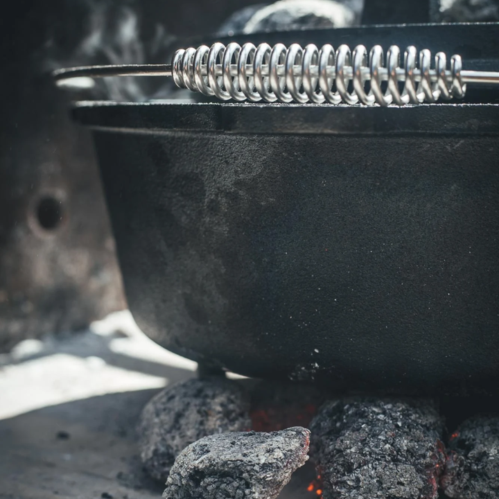 Zwarte kookpan van gietijzer met afneembare deksel en draaibare handgreep, geschikt voor kampvuur en grillen. Robuust ontwerp met drie poten voor stabiele kookstand.