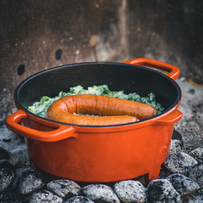Oranje kookpot met afdekking van The Windmill, een beperkte editie gietijzerpot met glazuur, geschikt voor kampvuur of hoge hitte. Perfect voor buitenkoken en grillen.