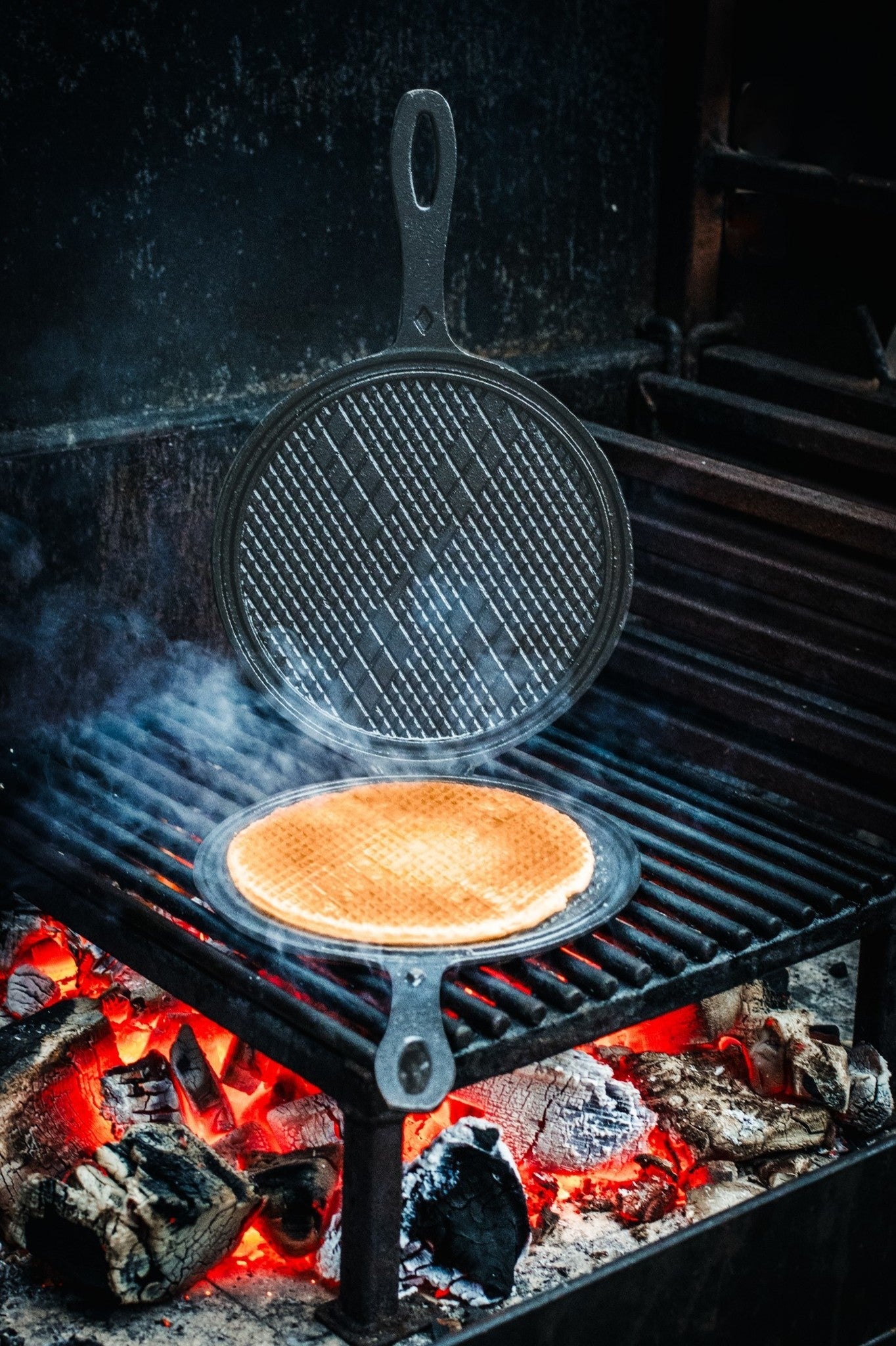 Zwarte, ronde wafelpan met opengeslagen deksel en gestructureerde grillvlakken. Gemaakt van kookstalen, geschikt voor het maken van wafels of broodjes.