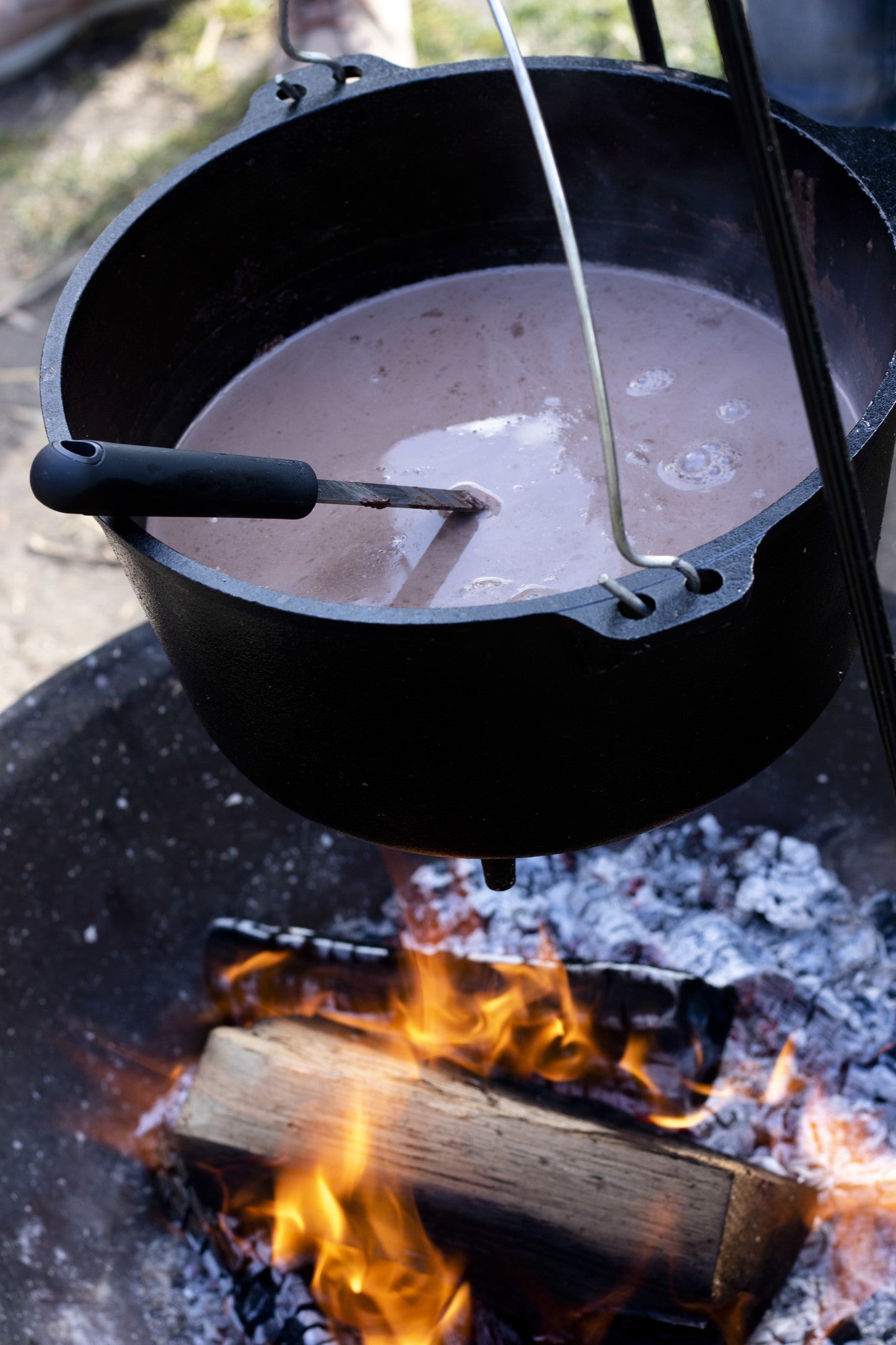 Zwarte hangende barbecue met grill en kookpan, voor buitenkeuken. Met decoratieve pootjes en metalen schepen, geschikt voor grillen en koken op de tuin.