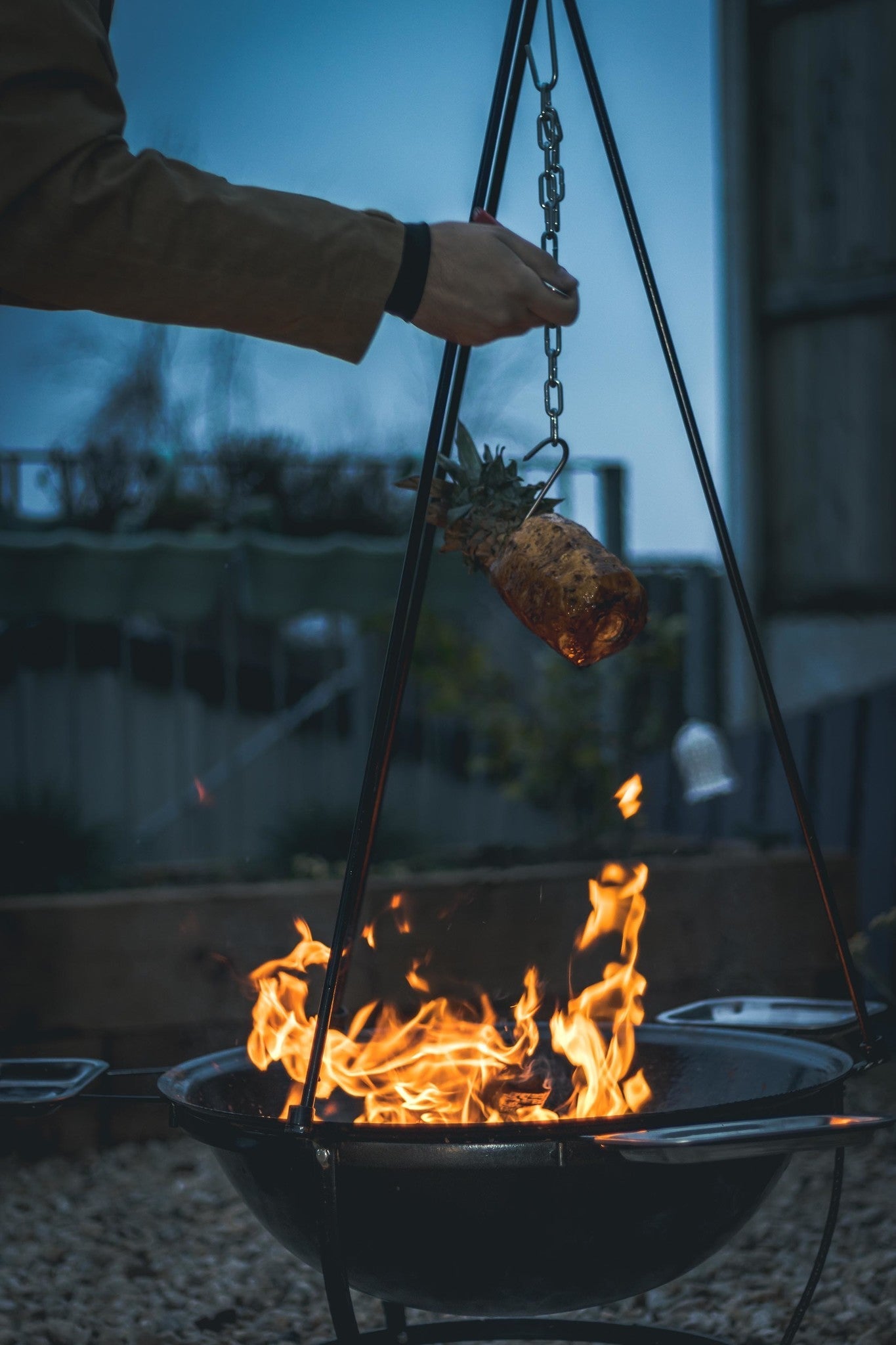 Zwarte hangende barbecue met grill en kookpan, voor buitenkeuken. Met decoratieve pootjes en metalen schepen, geschikt voor barbecuefeesten en grillavonden.