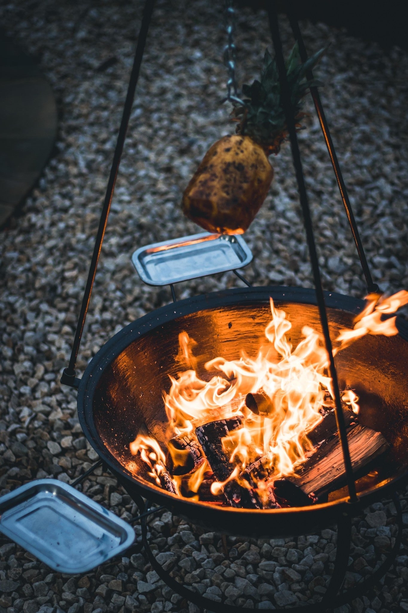 Zwarte hangende barbecue met grill en kookpan, voor buitenkeuken. Met decoratieve pootjes en metalen schepen, geschikt voor houtskoolbarbecue.