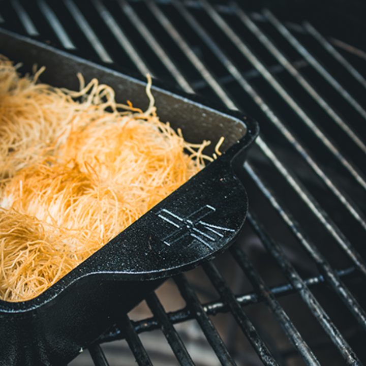 Zwarte, vierkante kookpan van gietijzer met geëmbosseerde handvatten en gladde binnenkant, geschikt voor oven- en grilltoepassingen. Robuust ontwerp voor professionele en thuiskeuken gebruik.
