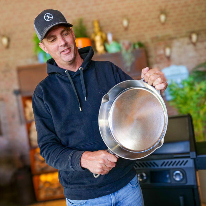 Een glanzende, zilverkleurige kookpan met een gladde bodem en twee handvatten, geschikt voor grillen en bakken. Gemaakt van roestvrij staal, ideaal voor professionele en thuiskeuken gebruik.