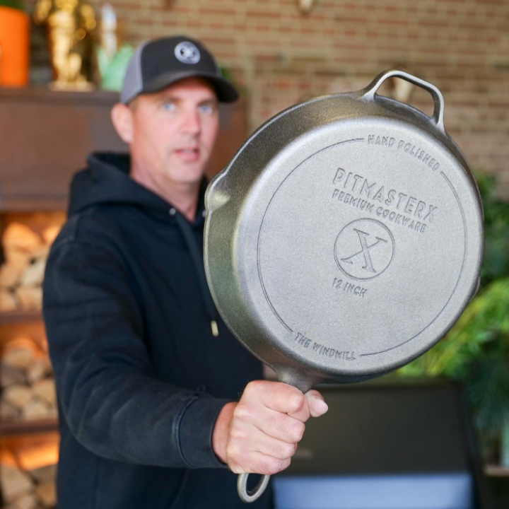 Een glanzende, zilverkleurige kookpan met een gladde bodem en een donkere, robuuste rand. De pan heeft een handvat en een kookrand, geschikt voor grillen en bakken.