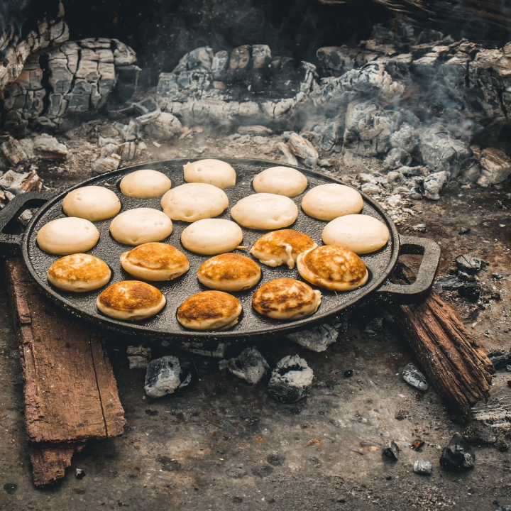 Zwarte, ronde cast-iron pannetje met twaalf bolvormige gaten, voor het bakken van traditionele Japanse takoyaki. Met handvatten aan weerszijden, geschikt voor gebruik op de kookplaat of in de oven.