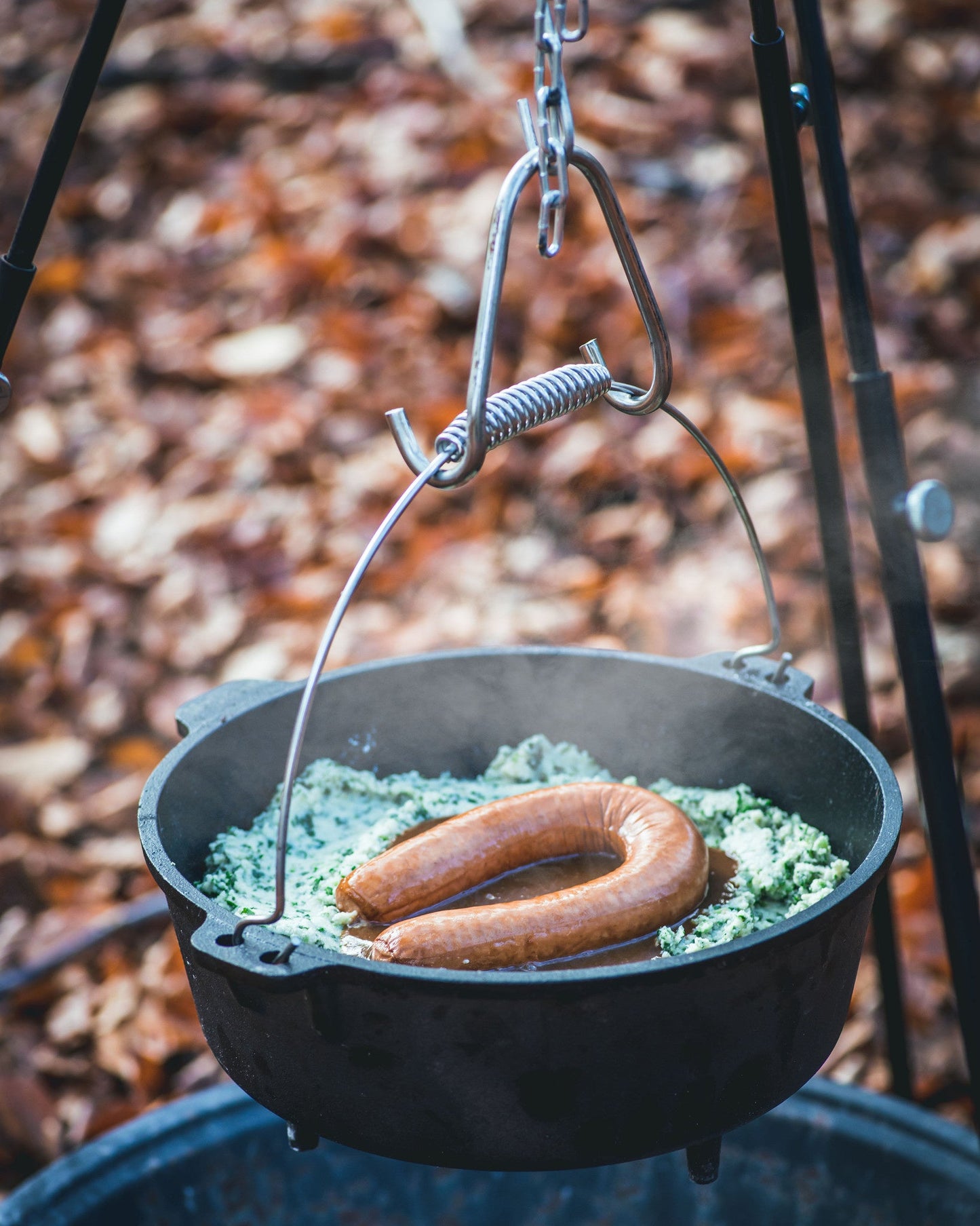 Zwarte kookpan van gietijzer met een stalen, opgerolde handgreep, geschikt voor kampvuur en barbecue. Robuust ontwerp voor outdoor koken en grillen.