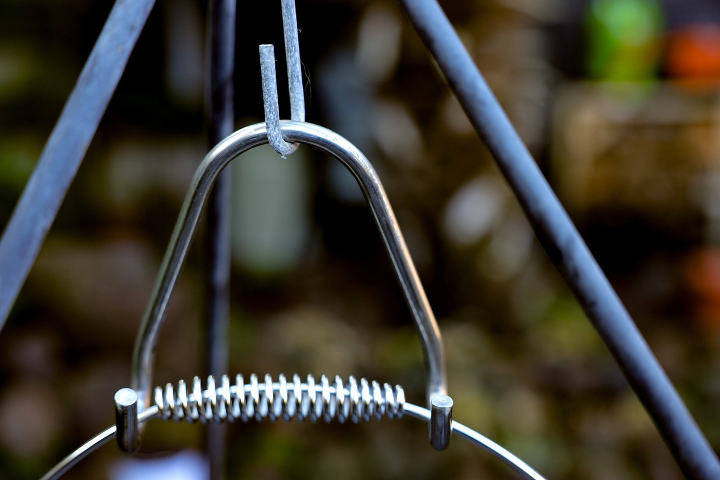 Zwarte kookpan van gietijzer met een zichtbare, zilverkleurige metalen handgreep en een springveerconstructie. Geschikt voor kampvuur en open haard, ideaal voor outdoor koken.