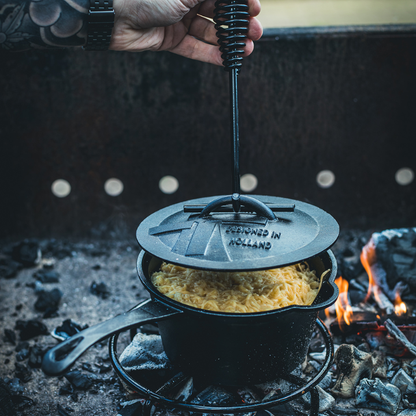 Zwarte kookpan van gietijzer met afsluitende deksel en handvat, geschikt voor kampvuur en houtkookplaat. Robuust ontwerp met duidelijke merkgravure en praktische handgrepen voor outdoor koken.