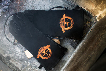 Zwarte leerhandschoenen met opgestikte goudkleurige logo, geschikt voor werken met warmte en hoge temperatuur. Zichtbare naadwerk en zachte textuur voor betere grip en comfort.