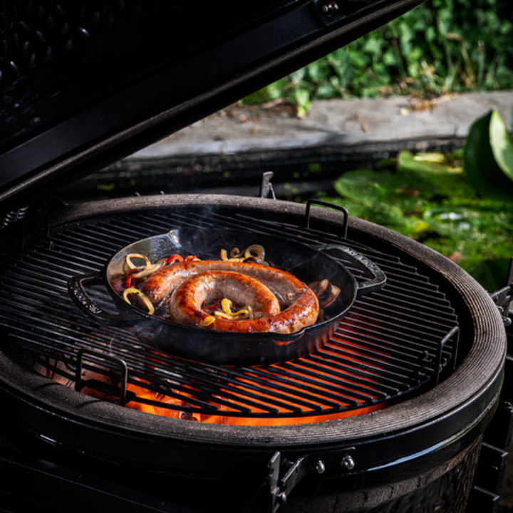 Zware, zwarte kookpan van gietijzer met twee handvatten en een gladde bodem, geschikt voor grillen en bakken. Perfect voor professionele en thuiskeuken gebruik.