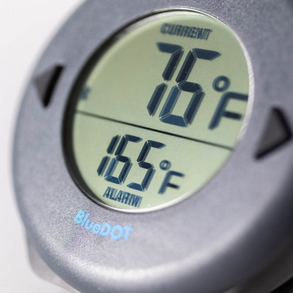 Zwart ronde BlueDOT thermometer met digitale display, toont huidige temperatuur 76°F en alarm 165°F. Bluetooth-icoon en bedieningsknoppen zichtbaar voor gebruik in keuken of op kookplaat.
