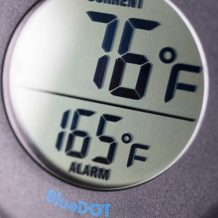 Zwart ronde BlueDOT thermometer met digitale display, toont huidige temperatuur 76°F en alarm 165°F. Bluetooth-icoon en bedieningsknoppen zichtbaar voor gebruik in keuken of op kookplaat.