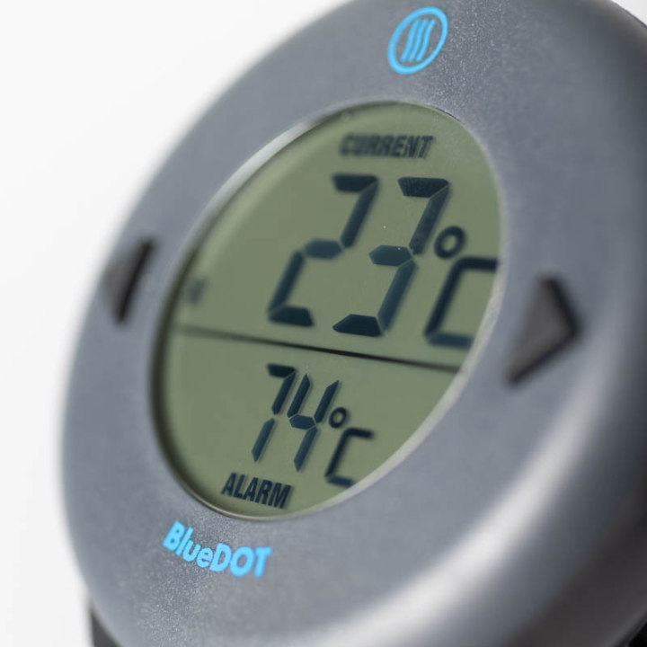 Zwart ronde BlueDOT thermometer met digitale display, toont huidige temperatuur 76°F en alarm 165°F. Bluetooth-icoon en bedieningsknoppen zichtbaar voor gebruik in keuken of op kookplaat.