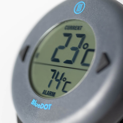 Zwart ronde BlueDOT thermometer met digitale display, toont huidige temperatuur 76°F en alarm 165°F. Bluetooth-icoon en bedieningsknoppen zichtbaar voor gebruik in keuken of op kookplaat.