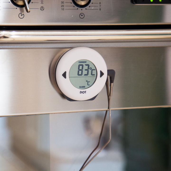 Een witte, ronde digitale temperatuurmeter met zwarte knoppen en een helder scherm dat 34°C huidtemperatuur en 75°C alarm toont. Geschikt voor medische of persoonlijke temperatuurcontrole.