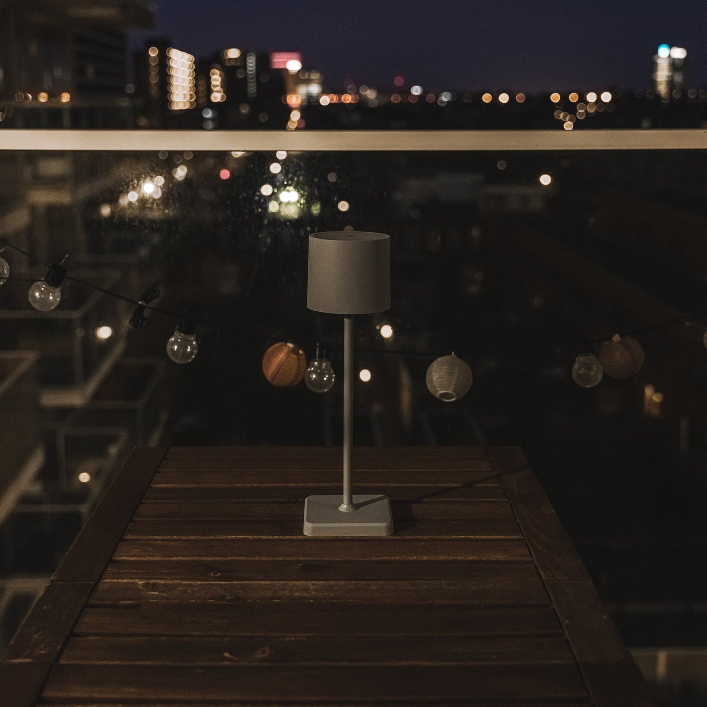 Een minimalistische grijze tafellamp met cilindrisch scherm en rechte steel, geschikt voor moderne slaapkamer- of woonruimteverlichting. Geïntegreerd in een strak, stijlvol design voor een rustige sfeer.