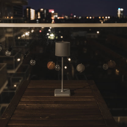 Een minimalistische grijze tafellamp met cilindrisch scherm en rechte steel, geschikt voor moderne slaapkamer- of woonruimteverlichting. Geïntegreerd in een strak, stijlvol design voor een rustige sfeer.