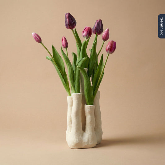 Een witte, textuurrijke keramische vaas met organische vormen, gevuld met paarse tulpen en groene bladeren, perfect voor moderne interieurs en decoratieve bloemstukken.