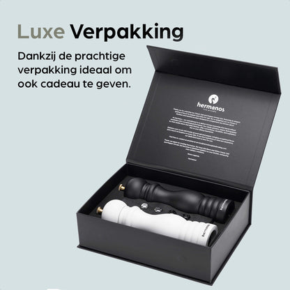 Een witte en zwarte houten pepermolen met goudkleurige doppen, geplaatst op een zwarte standaard met het merk 'hermanos'. Inclusief extra zilveren doppen voor keuken- en eetkamerdecoratie.
