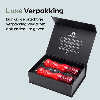 Rode houten pepermolen en zoutmolen van Hermanos, met glanzende goudkleurige doppen en een donkerrode basis. Ideaal voor keukengereedschap en kooktoestellen in een moderne keuken.