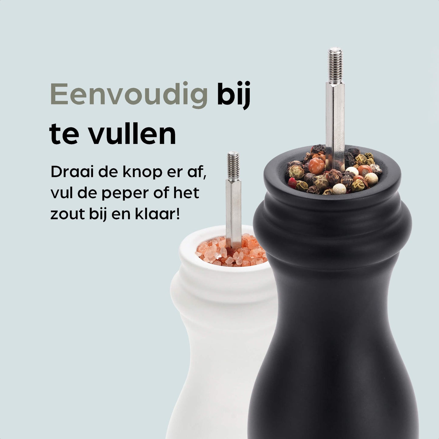 Een witte en zwarte houten pepermolen met goudkleurige doppen, geplaatst op een zwarte standaard met het merk 'hermanos'. Inclusief extra zilveren doppen voor keuken- en eetkamergebruik.