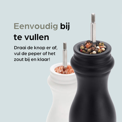 Een witte en zwarte houten pepermolen met goudkleurige doppen, geplaatst op een zwarte standaard met het merk 'hermanos'. Inclusief extra zilveren doppen voor keuken- en eetkamergebruik.