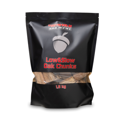 Zwarte verpakking met transparante onderkant, gevuld met houtblokken voor barbecue. Het merk ‘Vuurenrook.nl’ en de tekst ‘Low&Slow Oak Chunks’ zijn duidelijk zichtbaar.