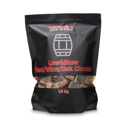 Zwarte verpakking met transparante bodem, gevuld met houtblokken voor roosteren. Rode tekst vermeldt 'Low&Slow Red/Wine/Oak Chunks' en gewicht 1,5 kg, geschikt voor barbecue en houtskoolbranding.