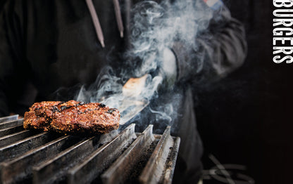 Een overvloedige, gegrilde BBQ-burger met kaas, bacon, ui en pepers op een houten snijplank, voor een brandend vuur. Award-winning recepten voor barbecue-enthusiasten.
