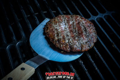 Een zilverkleurige, xtra lange roestvrijstalen burgerflipper met houten handvat, verpakt in zwarte blisterverpakking. Geschikt voor grillen en koken op de barbecue.